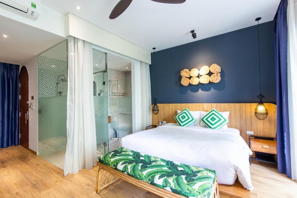 Habitación de hotel moderna con una cama grande, un banco, cabina de ducha de vidrio y una pared de acento oscura.