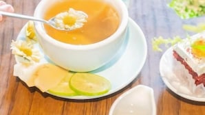 Uma mesa com uma tigela branca de chá, um jarro pequeno branco, e um prato com fatias de limão e uma flor.