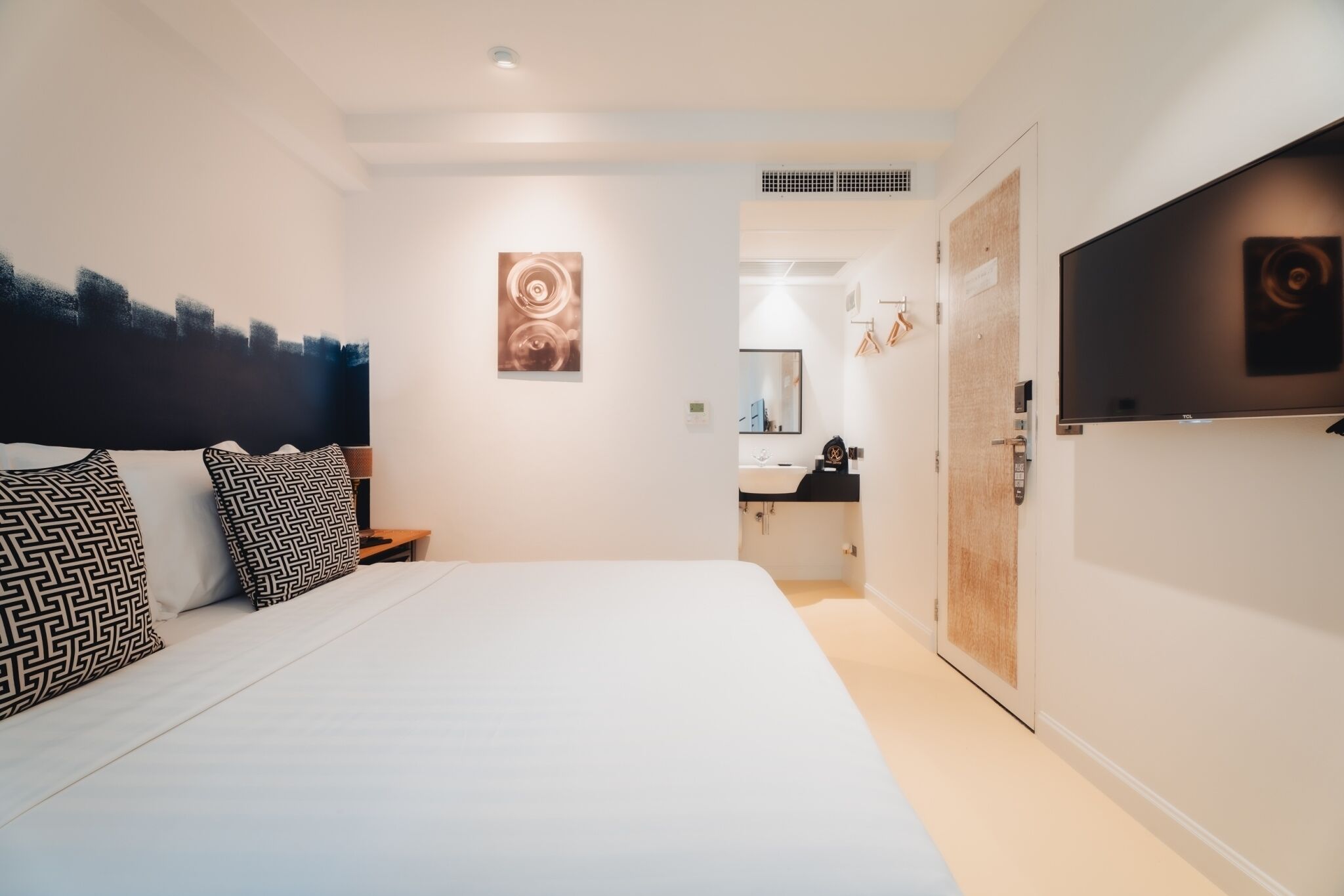 Moderni hotellihuone, jossa on suuri sänky, seinälle asennettu taulutelevisio ja pelkistetty sisustus.