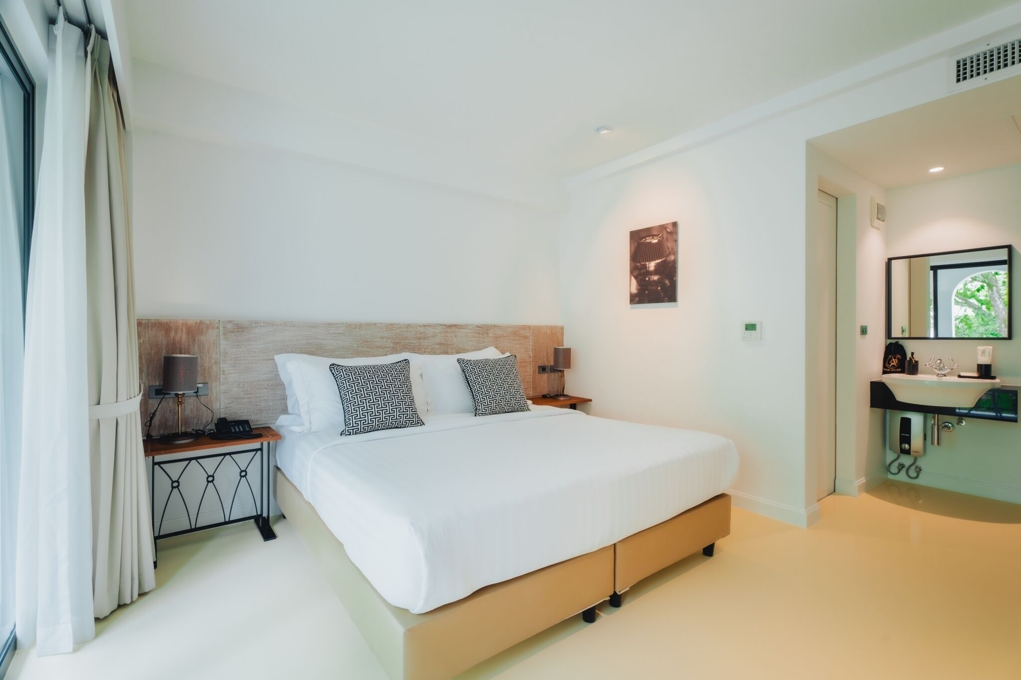 Une chambre d’hôtel moderne dotée d’un grand lit, de lampes de chevet, d’une table de chevet et d’une salle de bain avec un lavabo et un miroir, et offrant une vue sur l’extérieur.