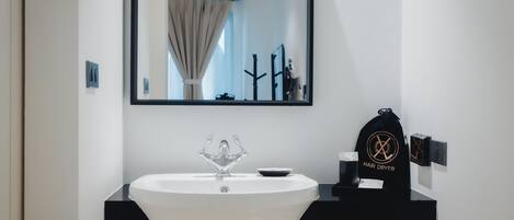 Une salle de bain moderne avec un lavabo blanc, un meuble-lavabo noir, un miroir et un sèche-cheveux fixé au mur.