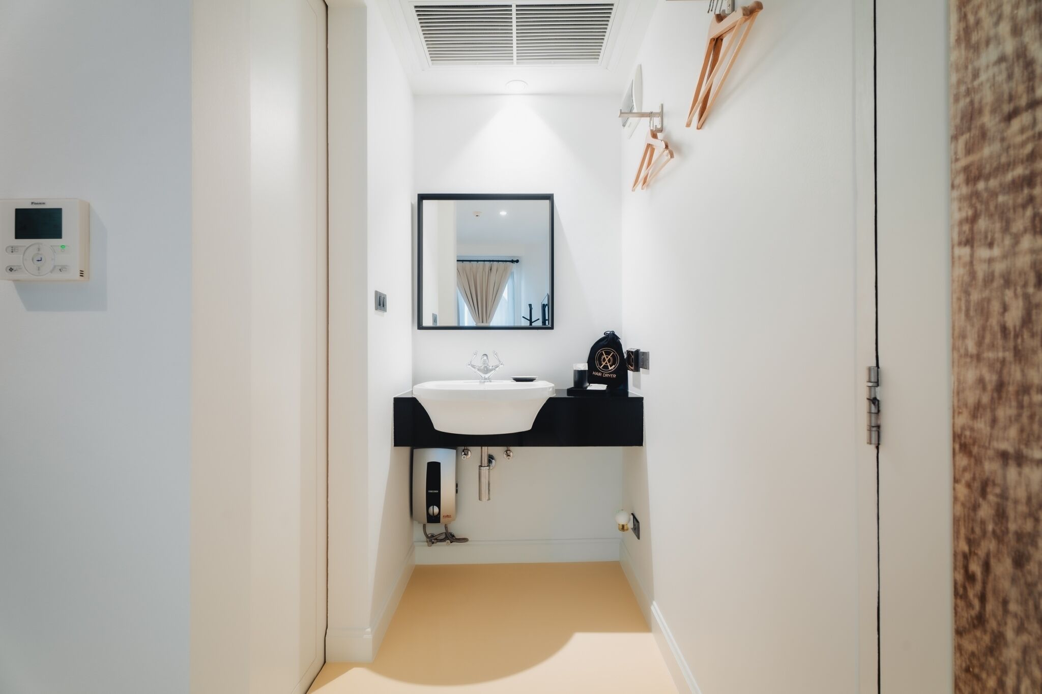 Une petite salle de bain avec un lavabo blanc, un miroir et une bouche d’aération au plafond.
