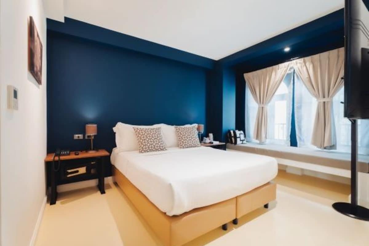Une chambre à coucher moderne avec un grand lit, une table de chevet, une lampe et une fenêtre avec des rideaux.