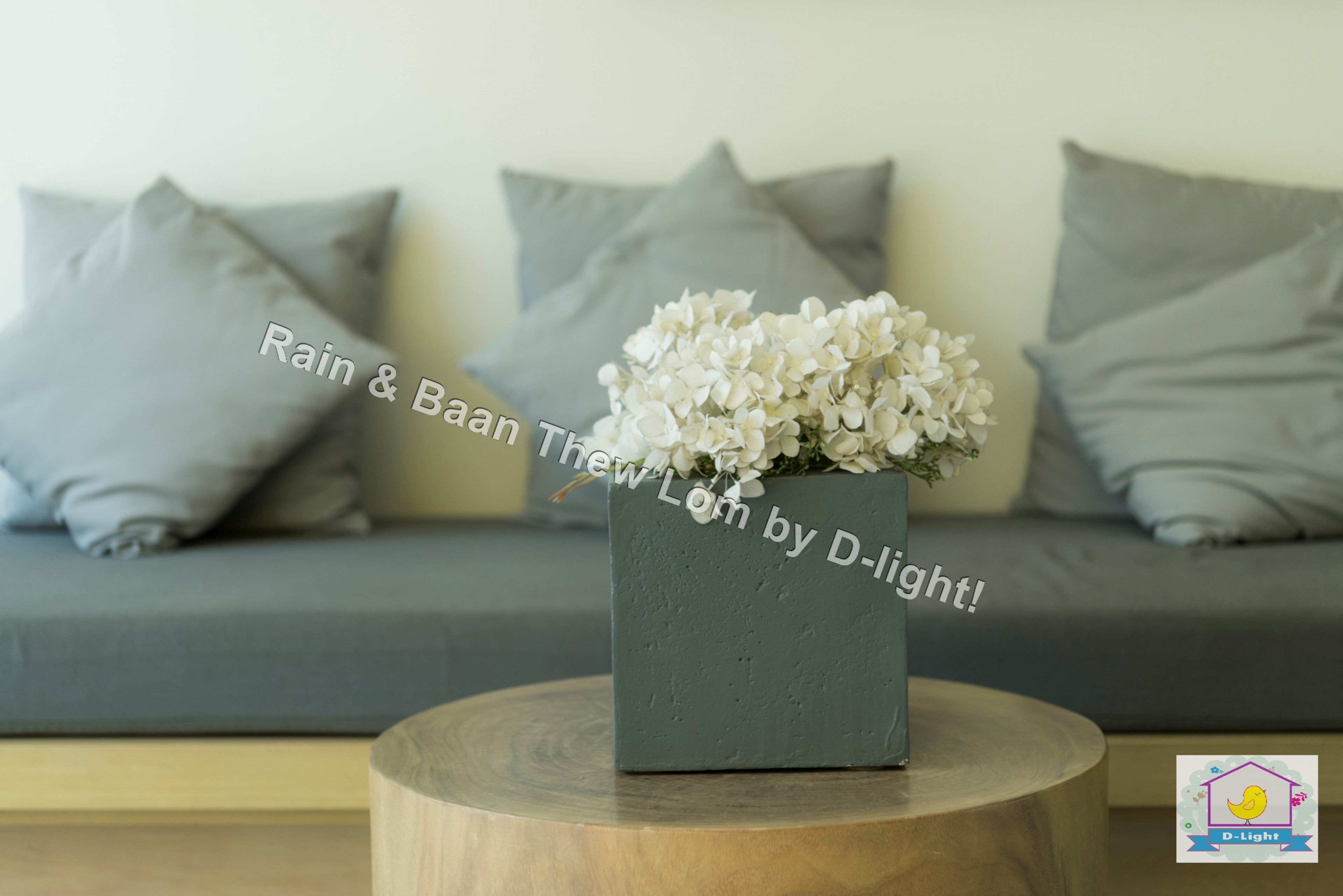 A grey sofa with grey cushions, a grey vase with white flowers, and a wooden stool.