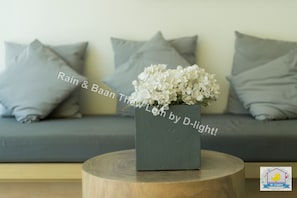 A grey sofa with grey cushions, a grey vase with white flowers, and a wooden stool. - Baan Thew Lom Cha-Am Huahin by D-light (Cha-am)