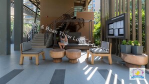 A modern outdoor seating area with wooden furniture and a staircase leading to an upper level. - Baan Thew Lom Cha-Am Huahin by D-light (Cha-am)