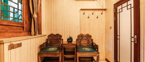 A traditional Japanese room with wooden paneling, two wooden chairs with green cushions, a small table, and a sliding door with a decorative handle.