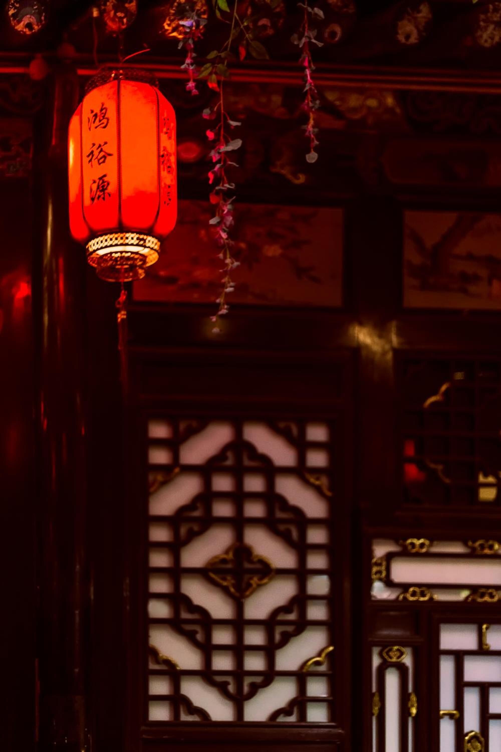 A traditional red lantern hanging in front of a wooden lattice window.