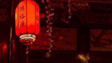 A traditional red lantern hanging in front of a wooden lattice window.