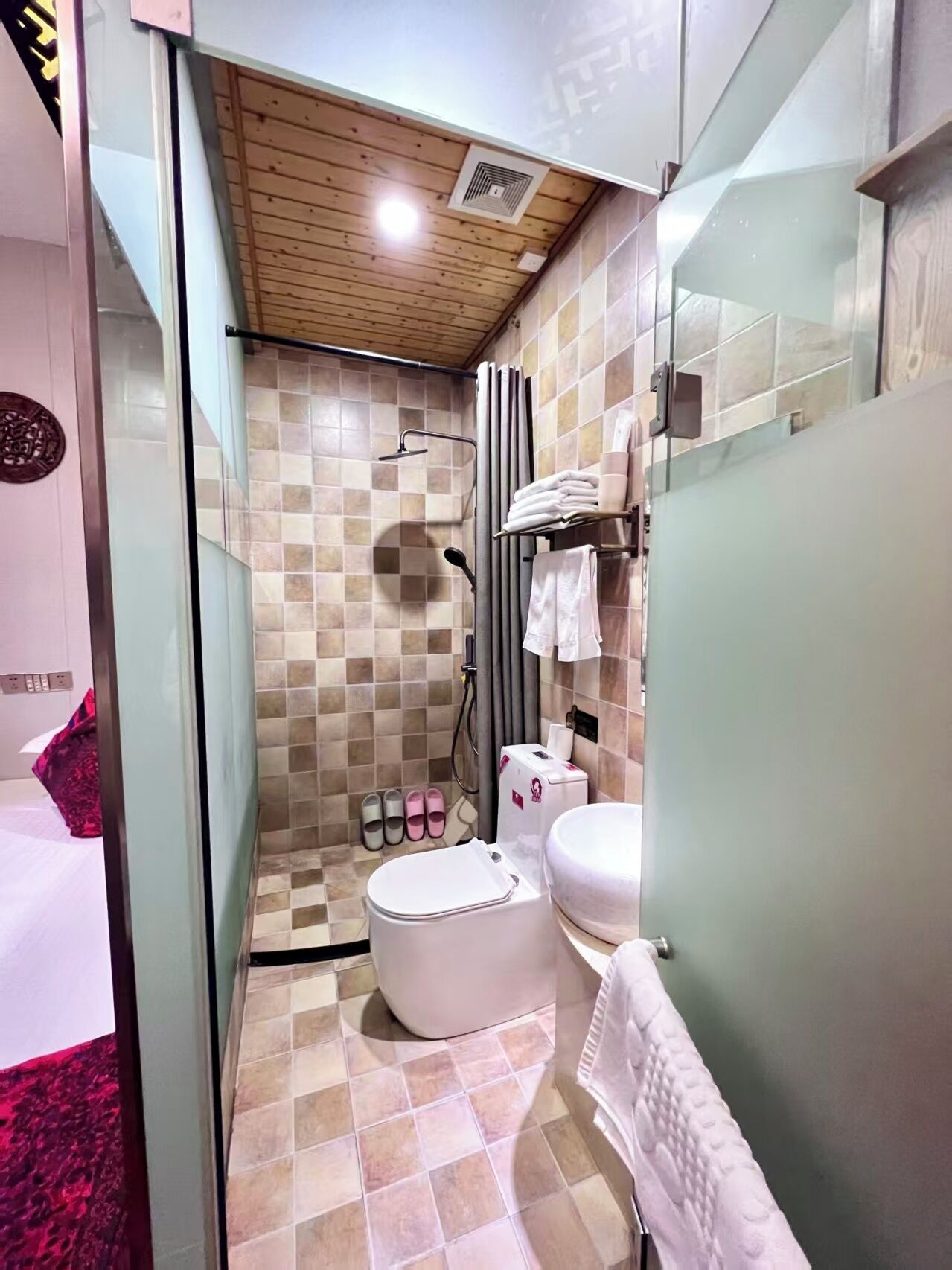 Un baño pequeño con ducha, inodoro y lavamanos, con baldosas de diseño ajedrezado y techo de madera.