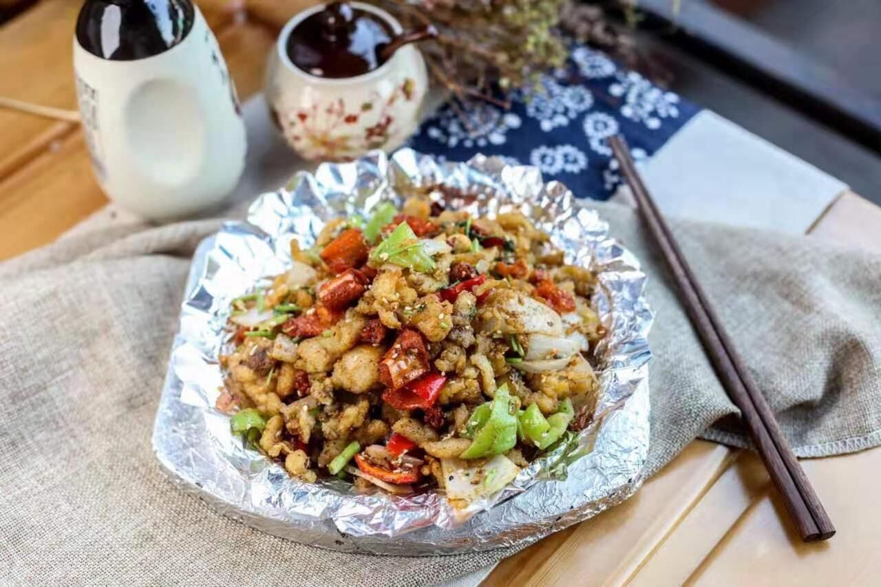 A meal served on aluminum foil with chopsticks and a cup of tea on a table.
