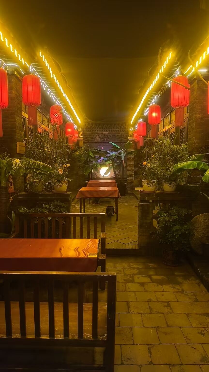 An outdoor dining area with red lanterns, potted plants, and a brick wall.