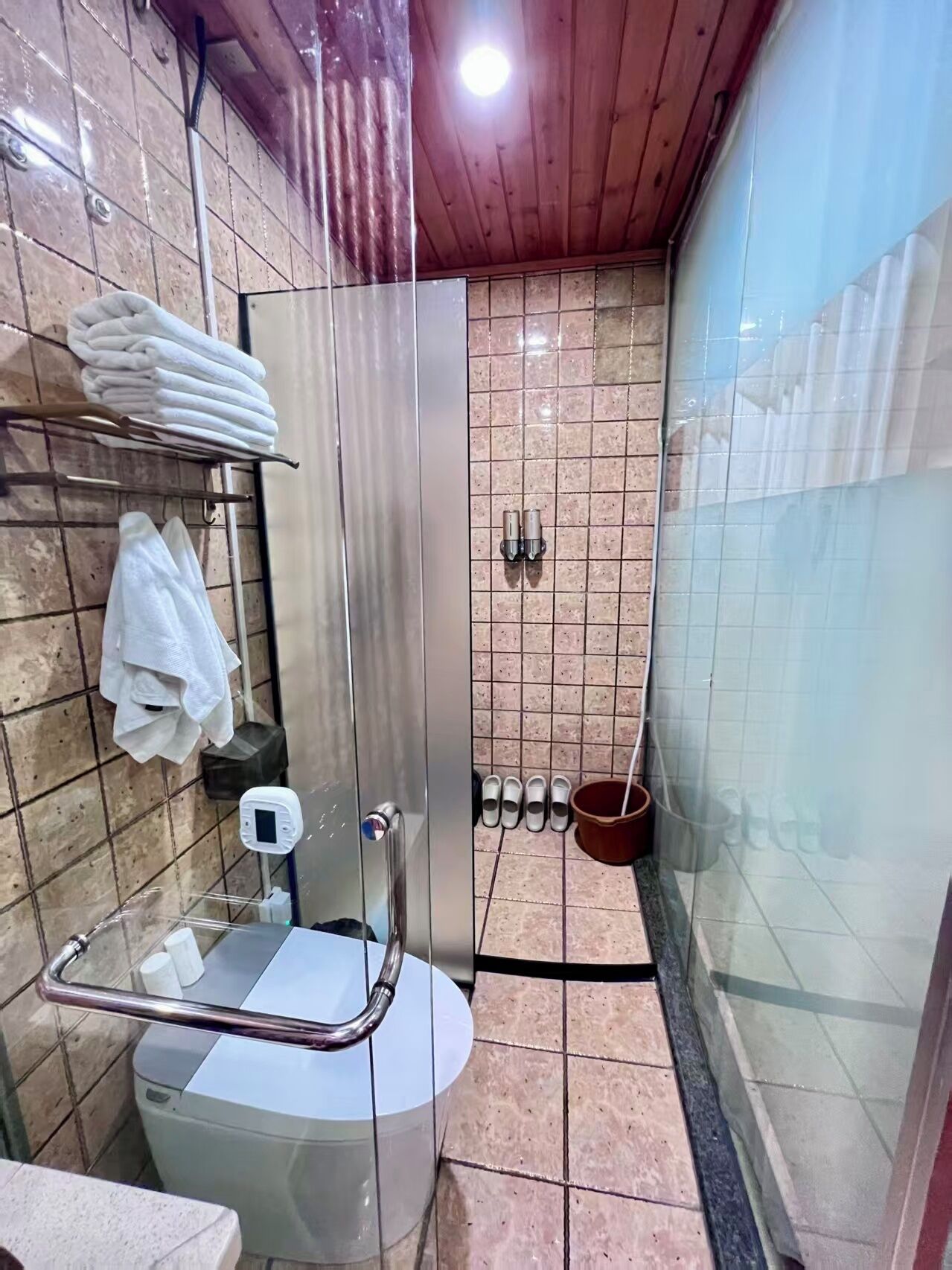 Un baño con inodoro, cabina de ducha de vidrio, toallero y dispensador de jabón en la pared.