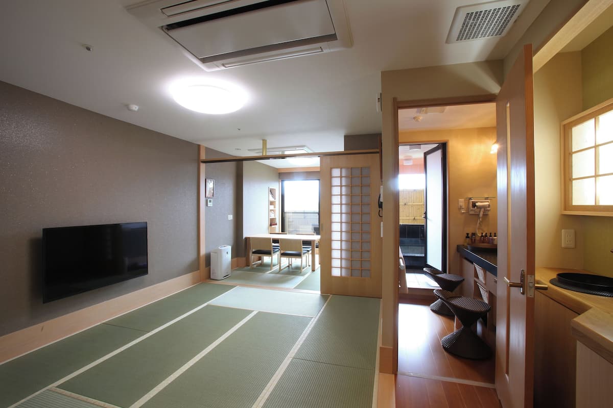A traditional Japanese room with tatami flooring, a television, a sliding door, and a small kitchen area.