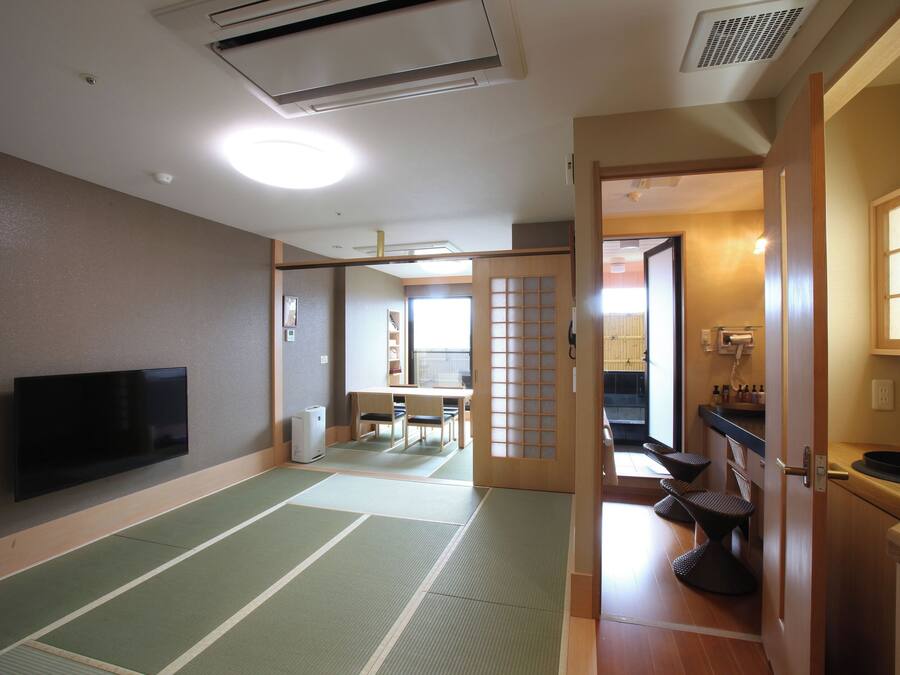 Una habitación japonesa tradicional con suelo de tatami, televisor, puerta corredera y una pequeña cocina.