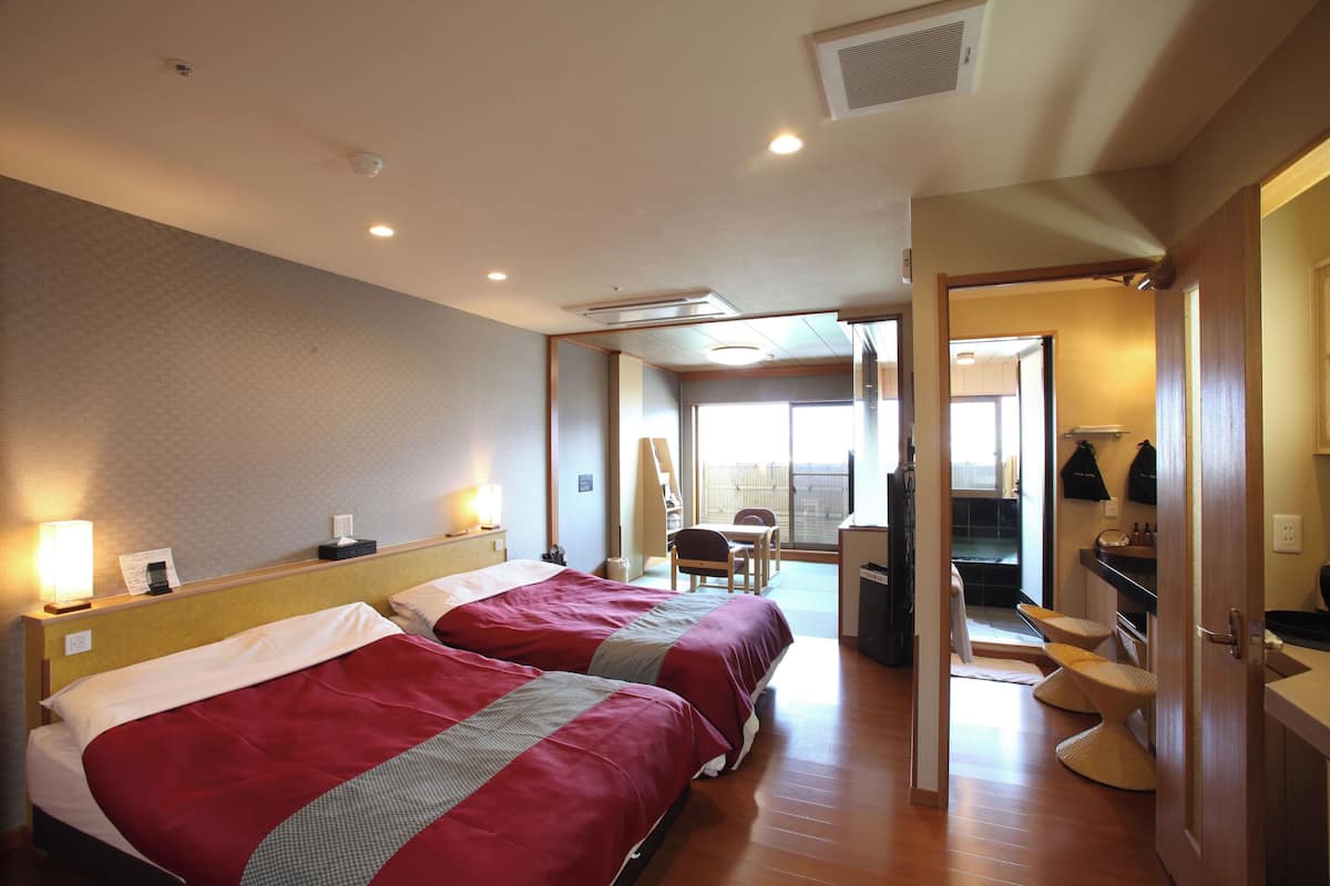 A hotel room with two beds, a desk, a chair, and a view of the outside.