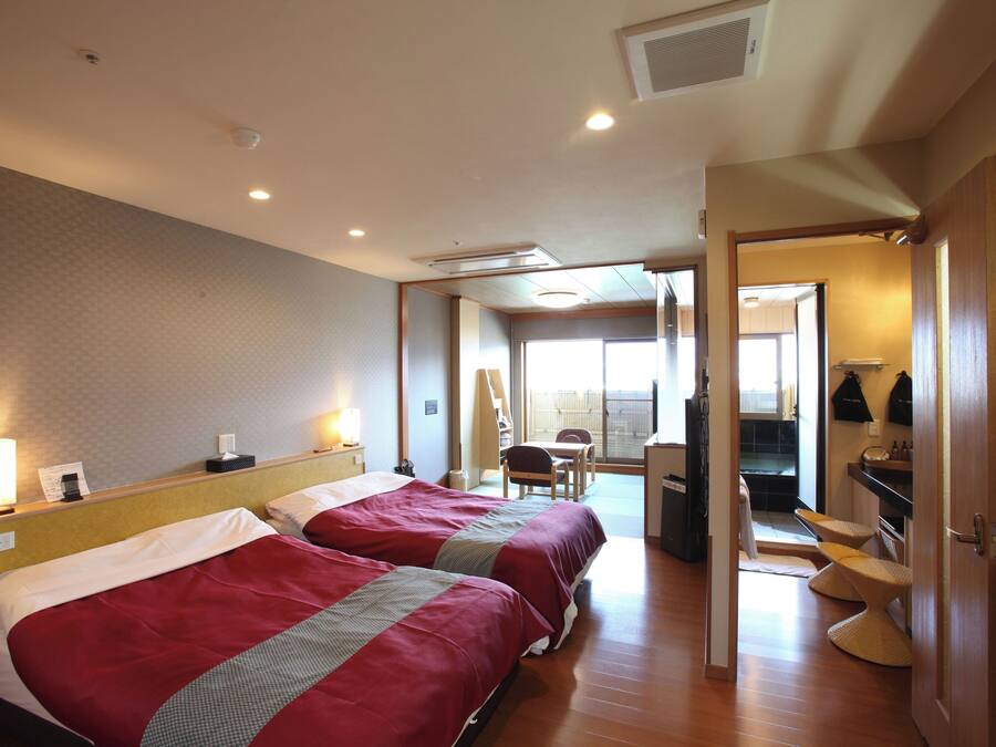A hotel room with two beds, a desk, a chair, and a view of the outside.