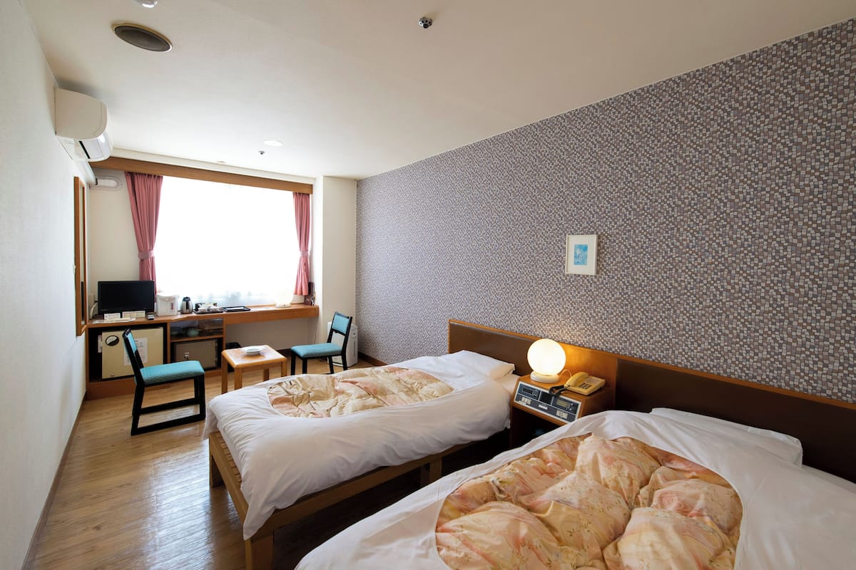 A hotel room with two beds, a desk with a computer, a chair, and a window with curtains.