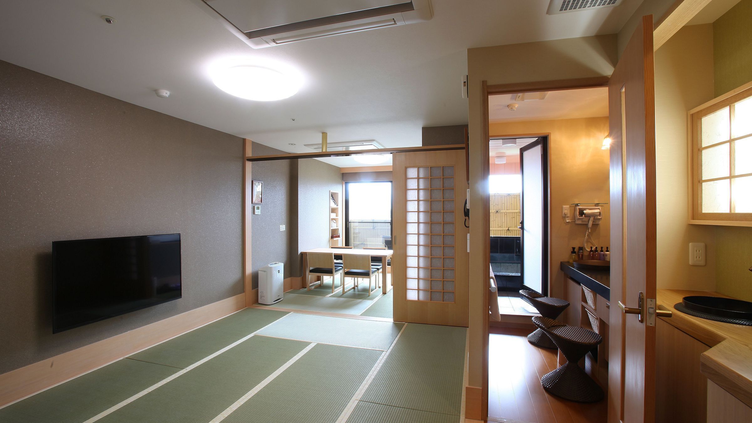 A traditional Japanese room with tatami flooring, a television, a sliding door leading to a balcony, and a small dining area.