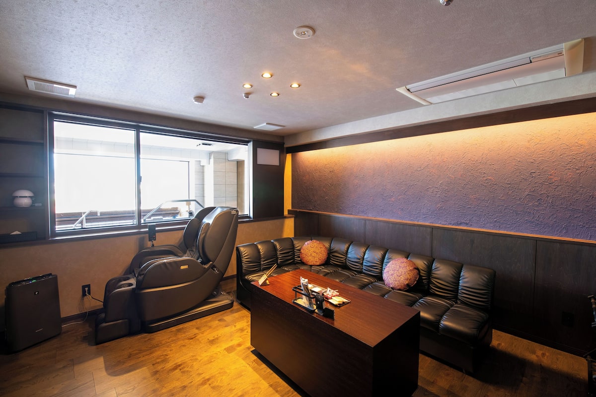 A modern room with a massage chair, a sofa with decorative pillows, and a wooden coffee table.