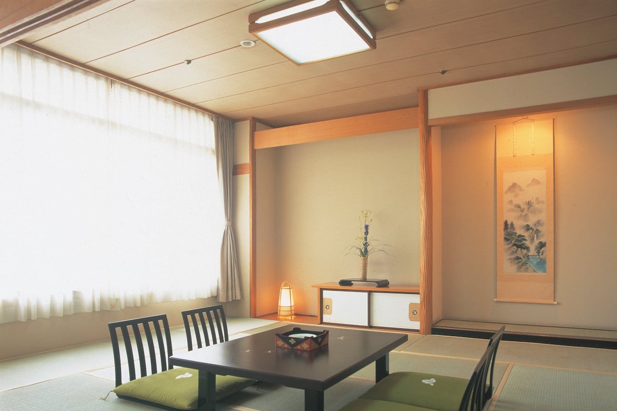 A traditional Japanese tatami room with a low table, chairs, and cushions.