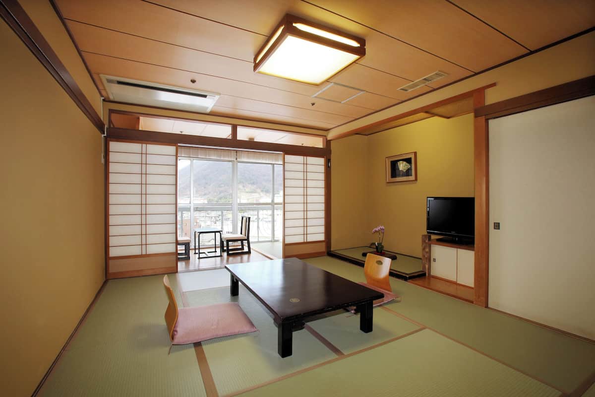 A traditional Japanese room with tatami flooring, a low table, a television, and sliding doors leading to a balcony.