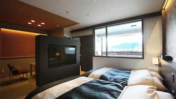 A modern hotel room with a large bed, a television, and a view of the outdoors through a large window.