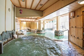 A traditional Japanese onsen with stone flooring, wooden beams, and a hot spring in the foreground. - Hanayagi No Sho Keizan (Fuefuki)