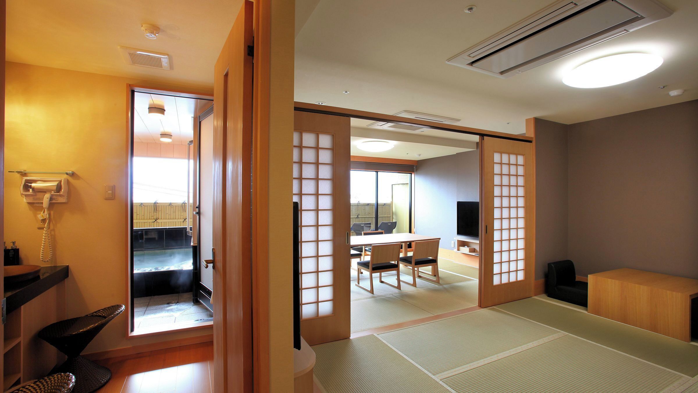 Ein traditioneller japanischer Raum mit Tatami-Böden, einem Fernseher, einem Telefon und einer Schiebetür, die zu einem Balkon führt.