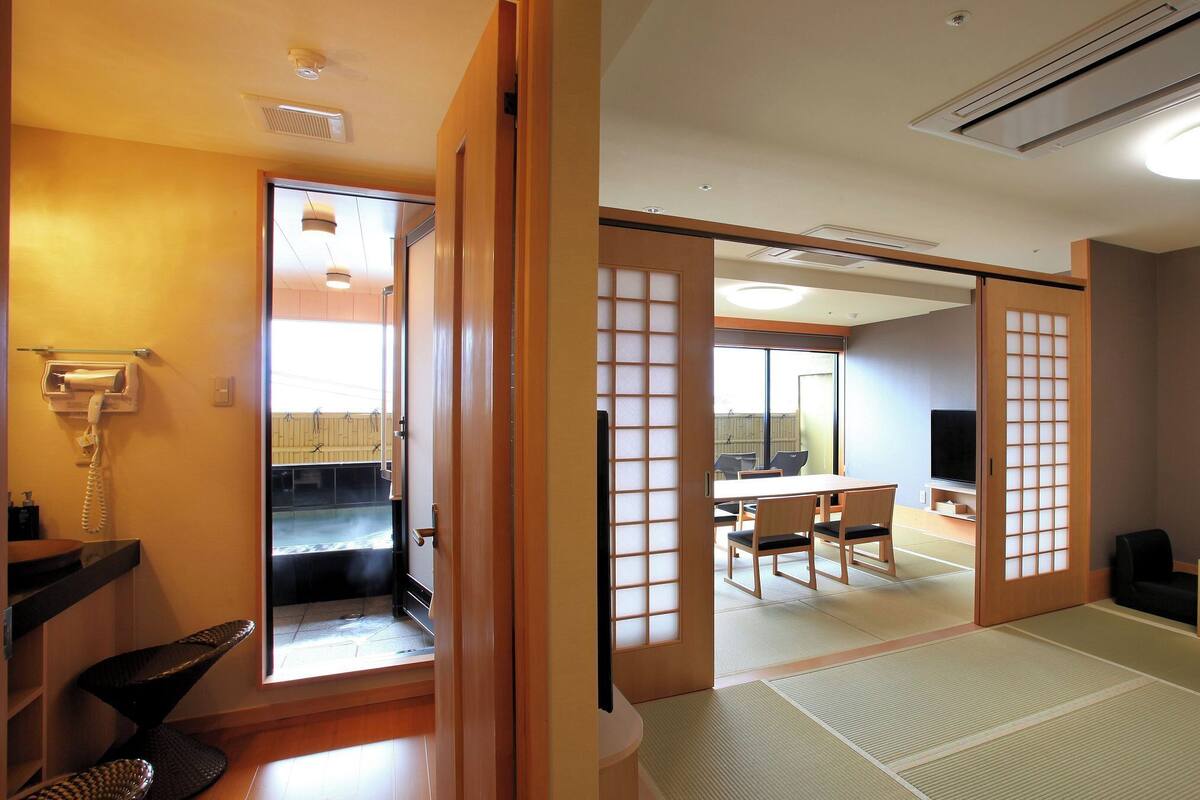 A traditional Japanese room with tatami flooring, a television, a telephone, and a sliding door leading to a balcony.