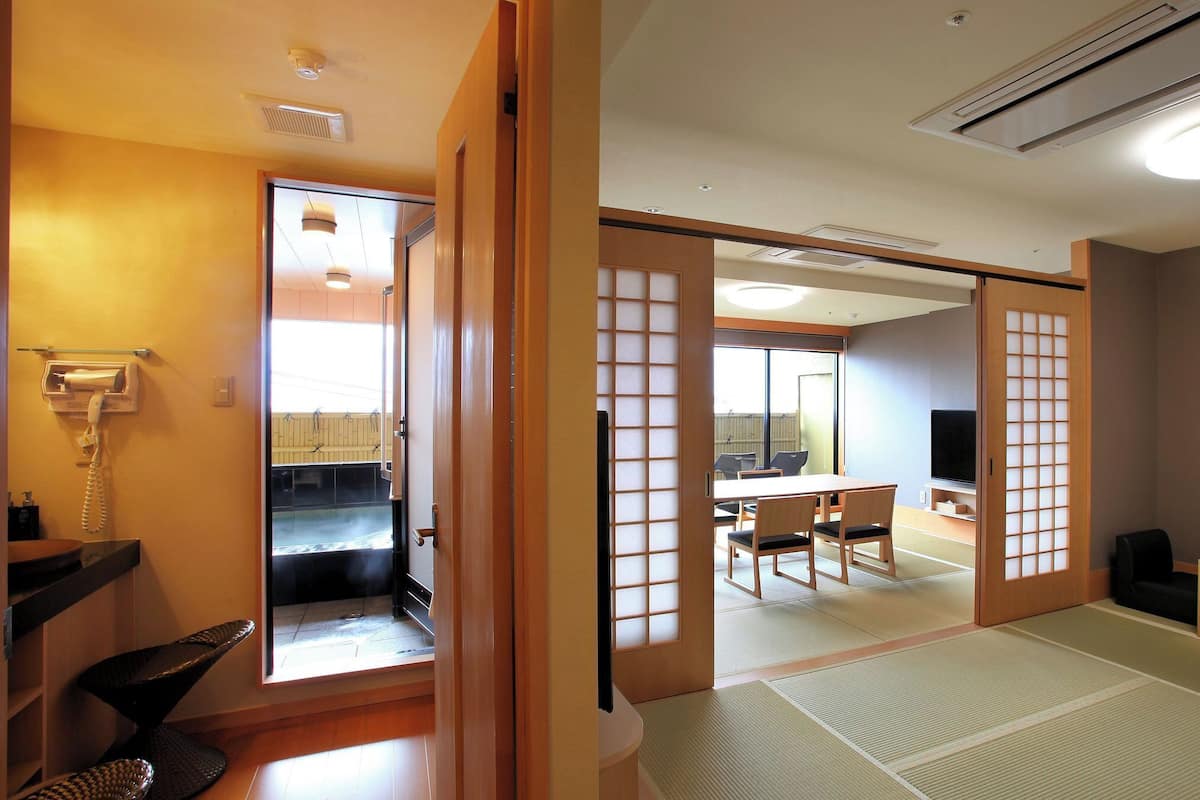Una habitación japonesa tradicional con suelo de tatami, televisor, teléfono y una puerta corredera que da a un balcón.