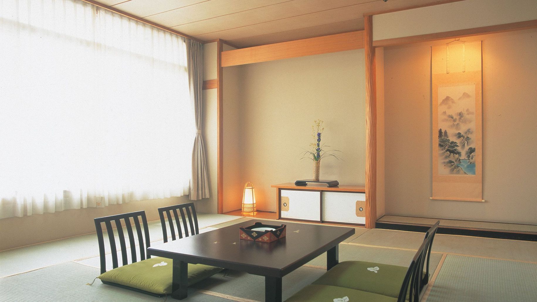 A traditional Japanese room with tatami flooring, a low table, chairs, a small table with a vase, and a painting on the wall.