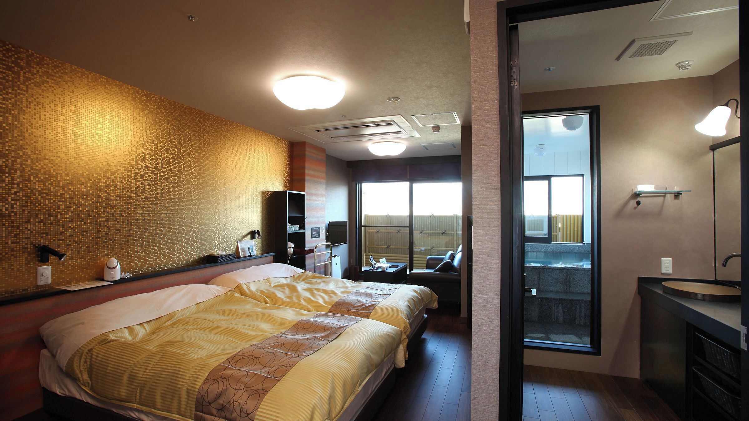 Ein Hotelzimmer mit Bett, Schreibtisch, Stuhl, großem Fenster und einem Badezimmer mit Spiegel und Waschbecken.