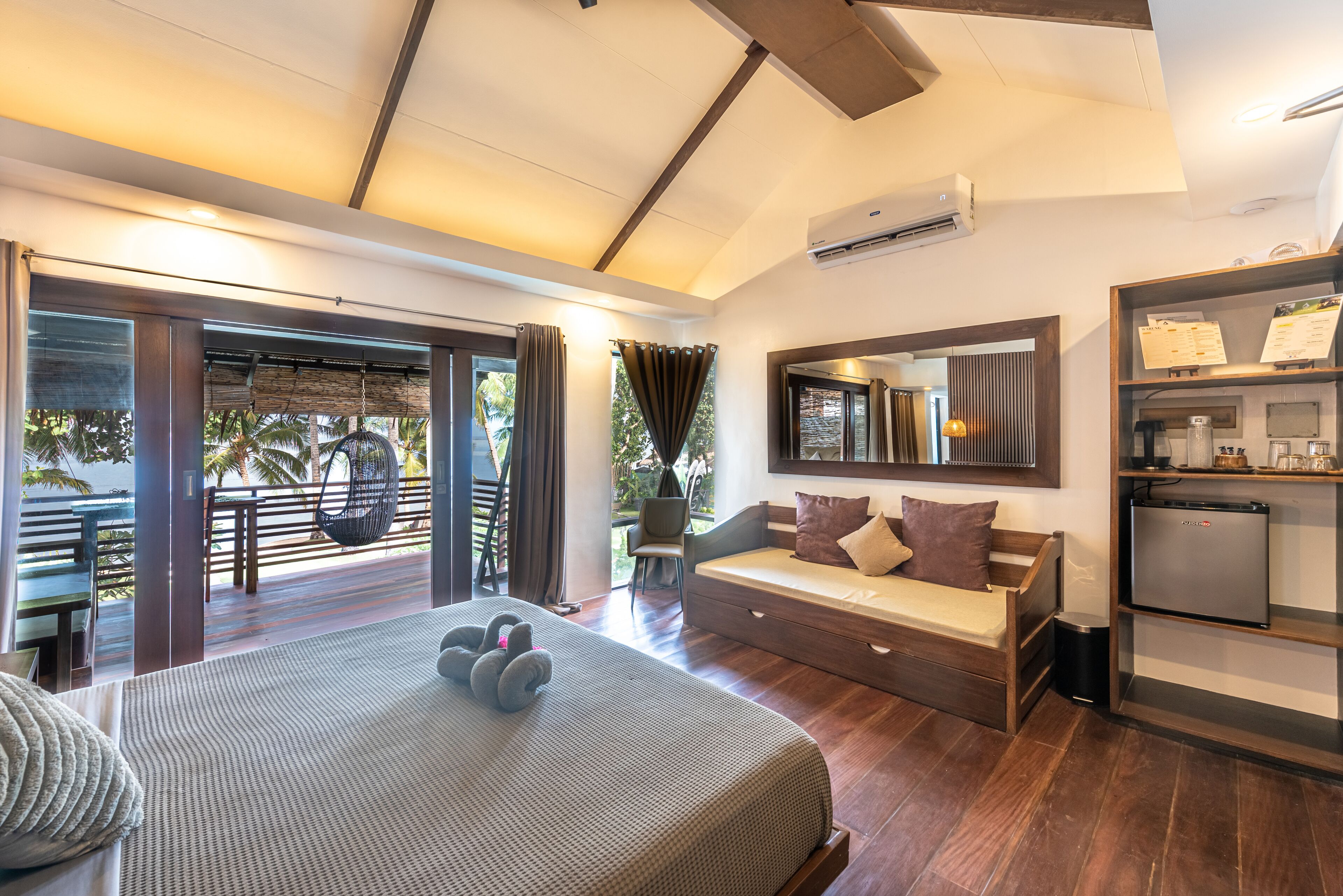 Quarto de hotel moderno com uma cama grande, um sofá, uma mesinha, um espelho e uma cozinha compacta.