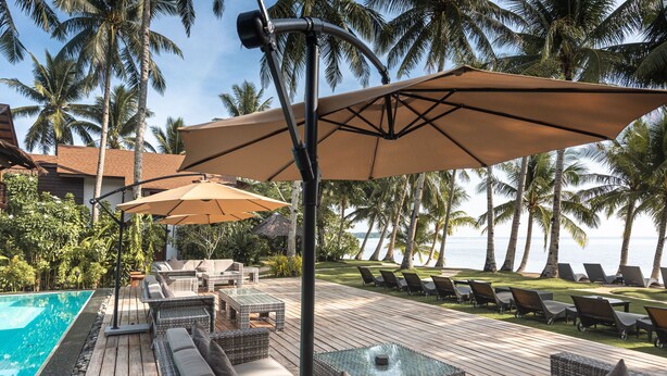 A poolside area with lounge chairs, a wooden deck, and umbrellas. - Siargao Island Villas (General Luna)