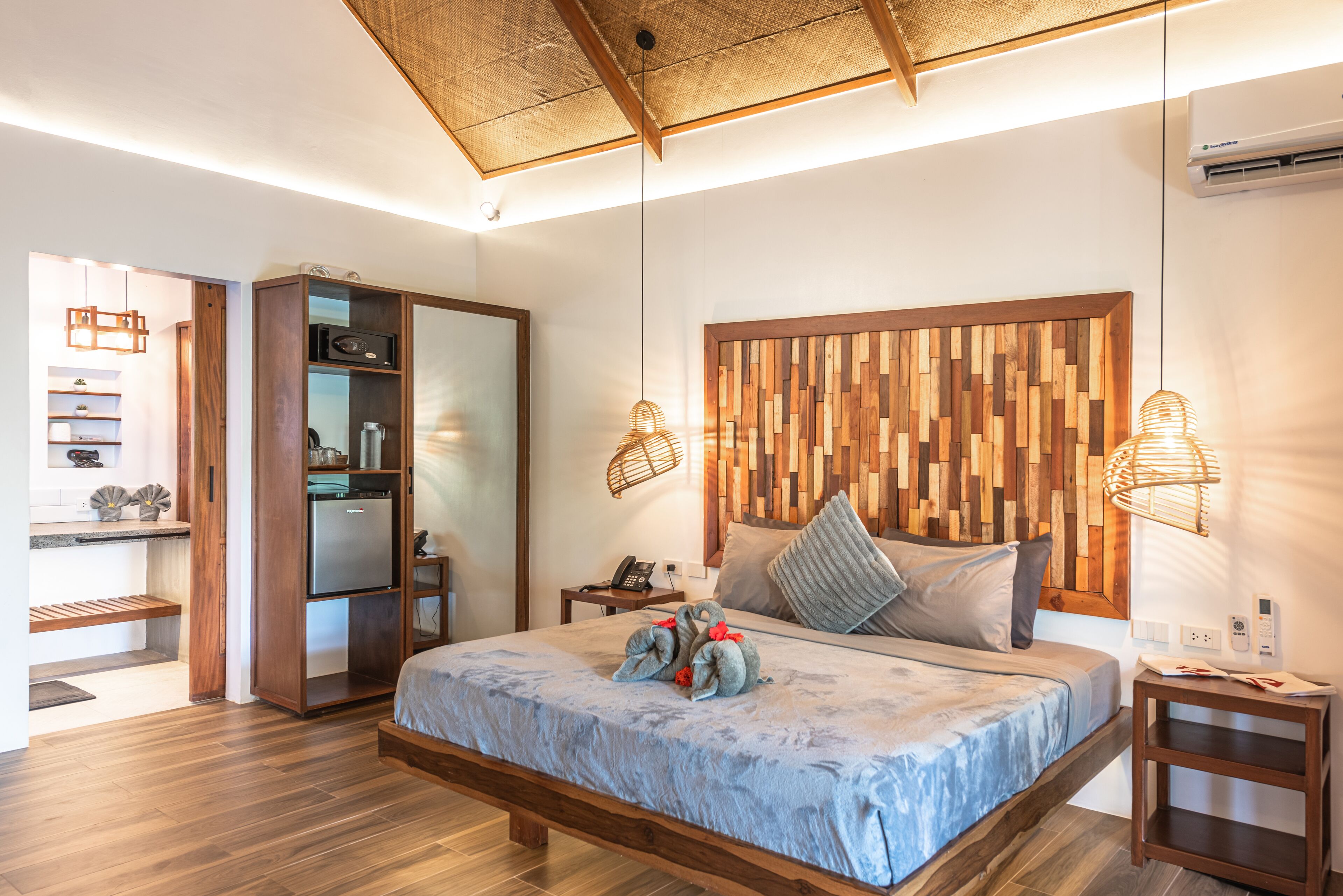 Un dormitorio moderno con cabecera de madera, una cama grande con colcha azul, un armario empotrado y una mesita de noche con lámpara.