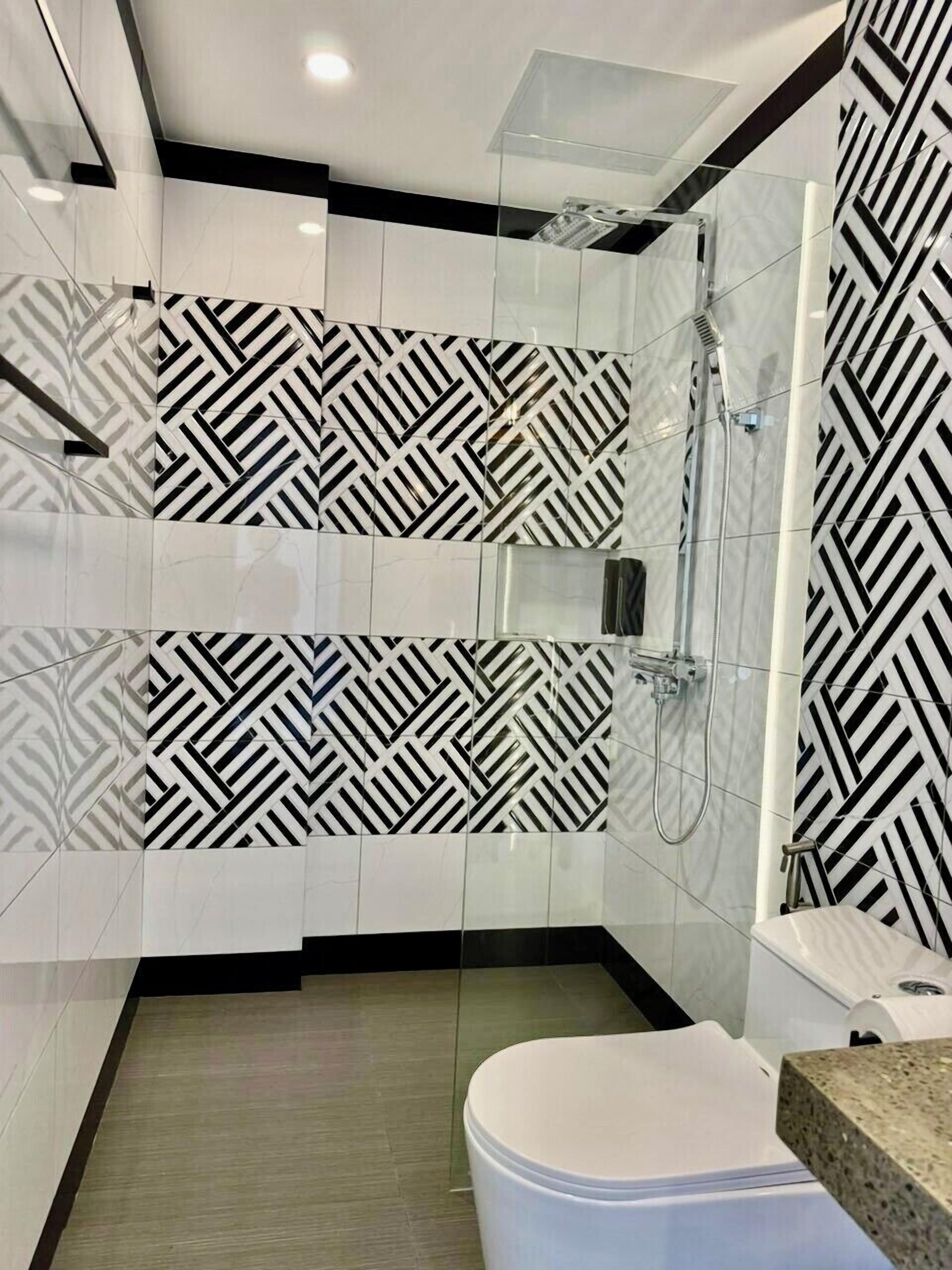 A modern bathroom with a geometric black and white tile pattern, a glass shower enclosure, and a white toilet.