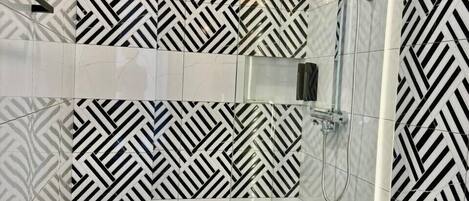 A modern bathroom with a geometric black and white tile pattern, a glass shower enclosure, and a white toilet.