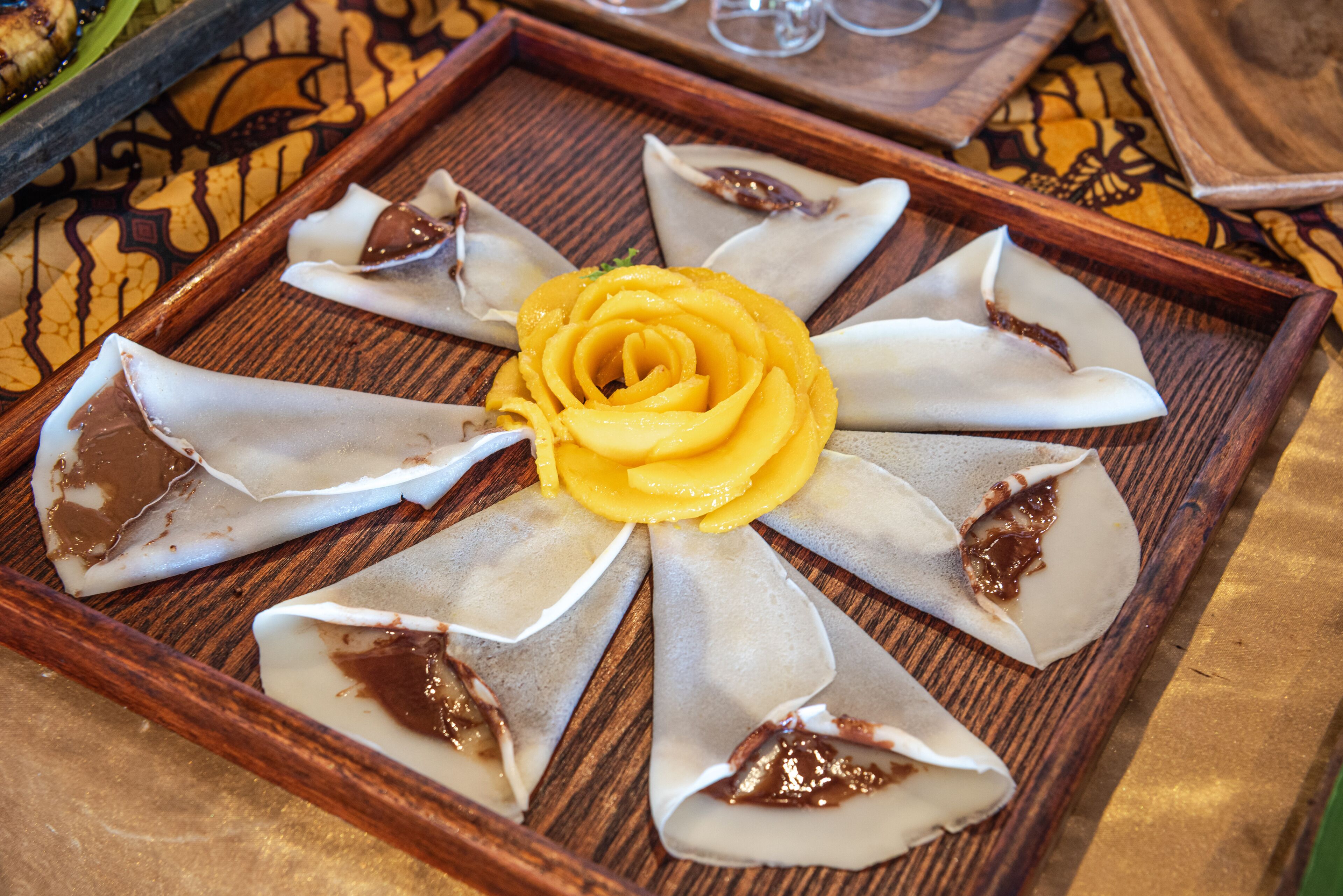 A wooden tray with a floral arrangement of food items.