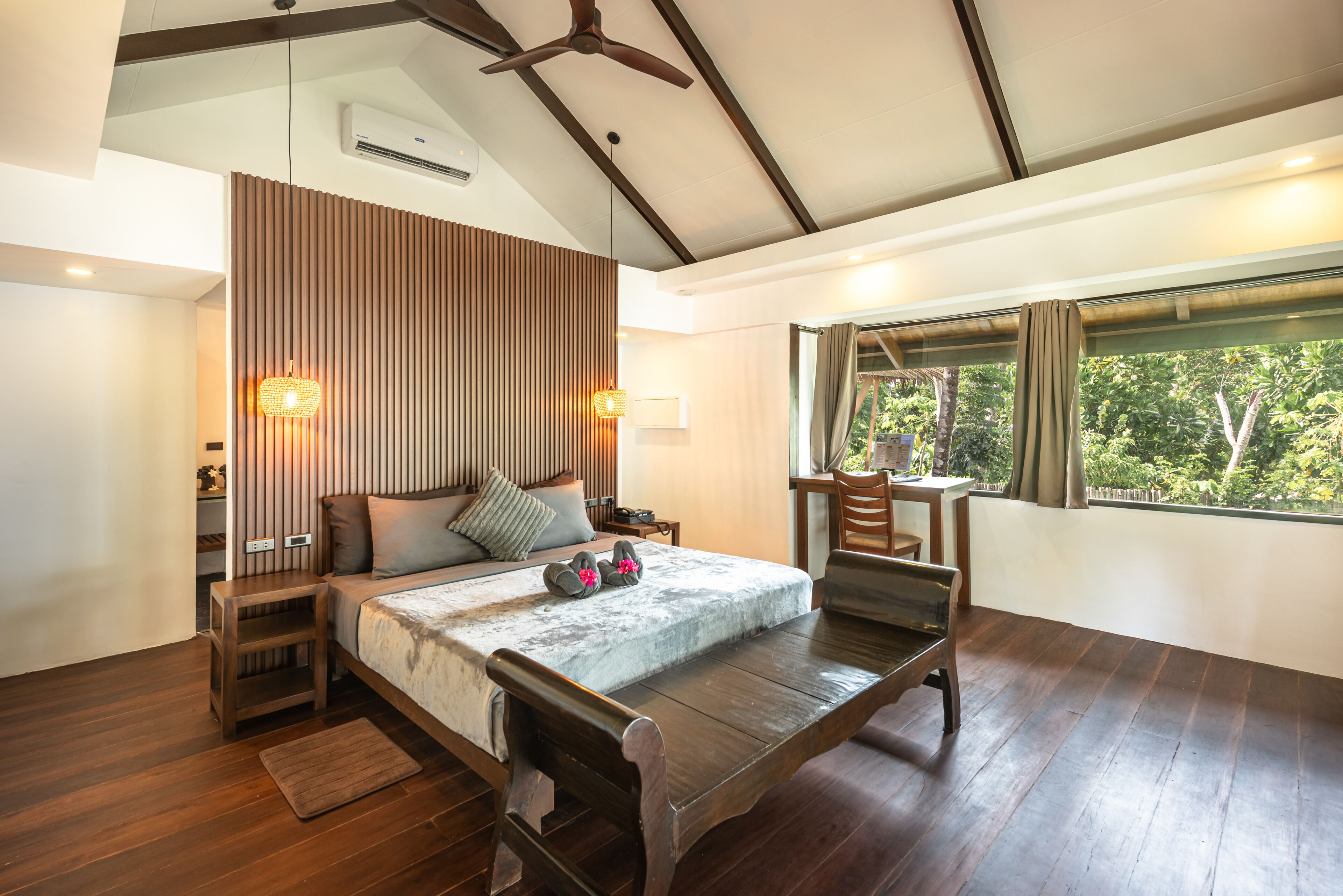 A modern bedroom with a bed, bedside tables, a desk, and a window with a view of greenery.