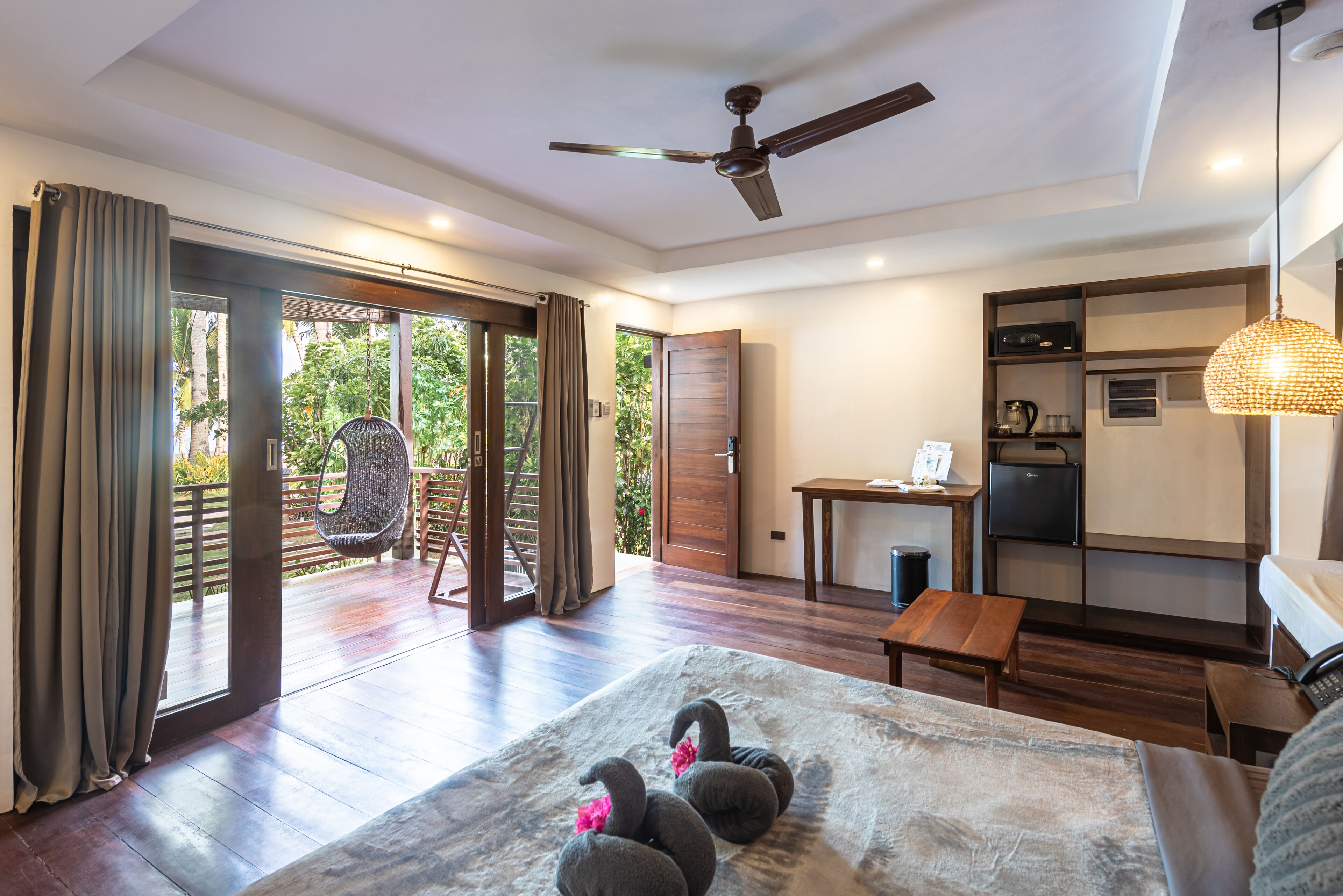 A modern hotel room with a large bed, a ceiling fan, a dining area, and a view of the outdoors.