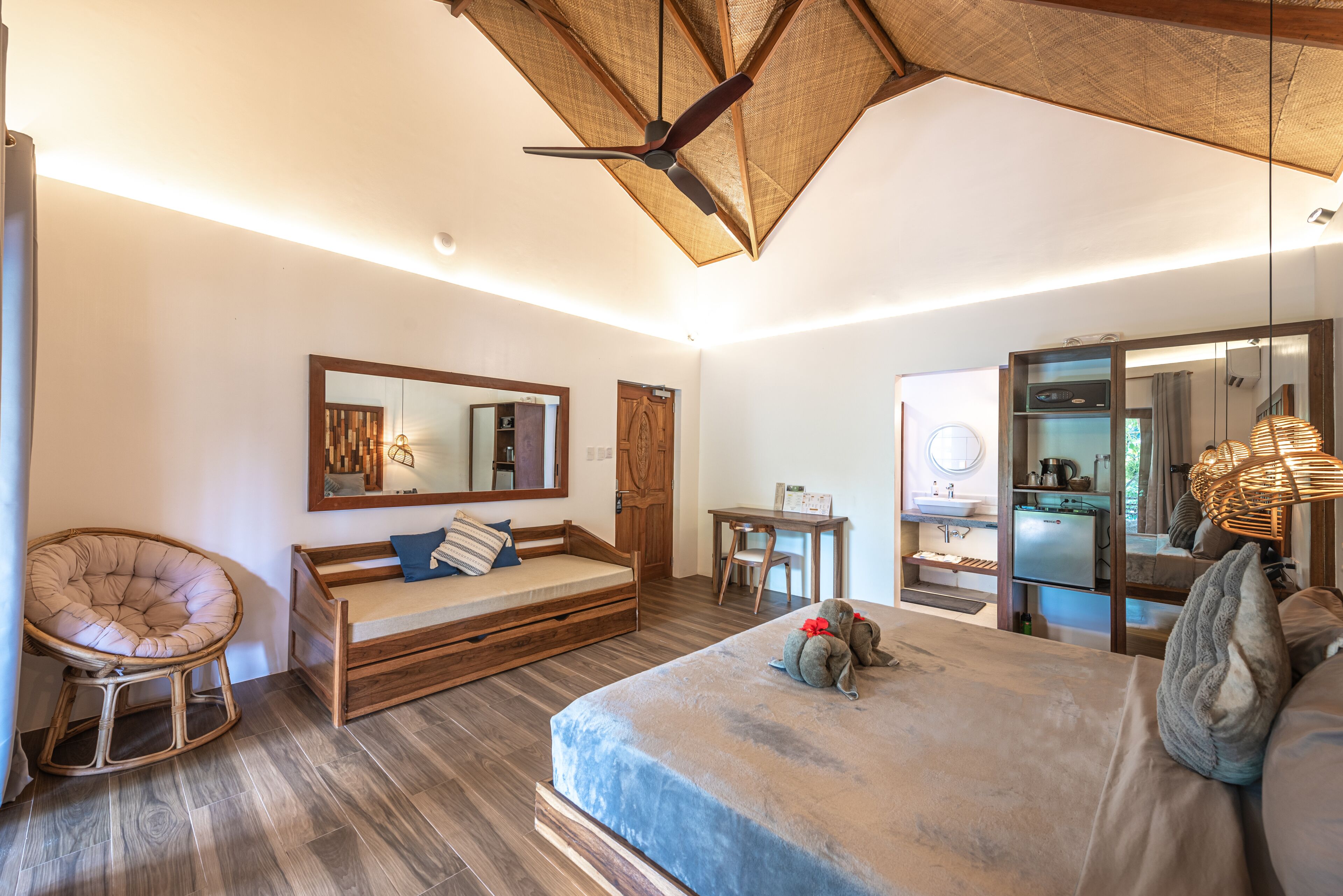 A modern bedroom with a bed, a wooden chair, a small desk, and a kitchenette.