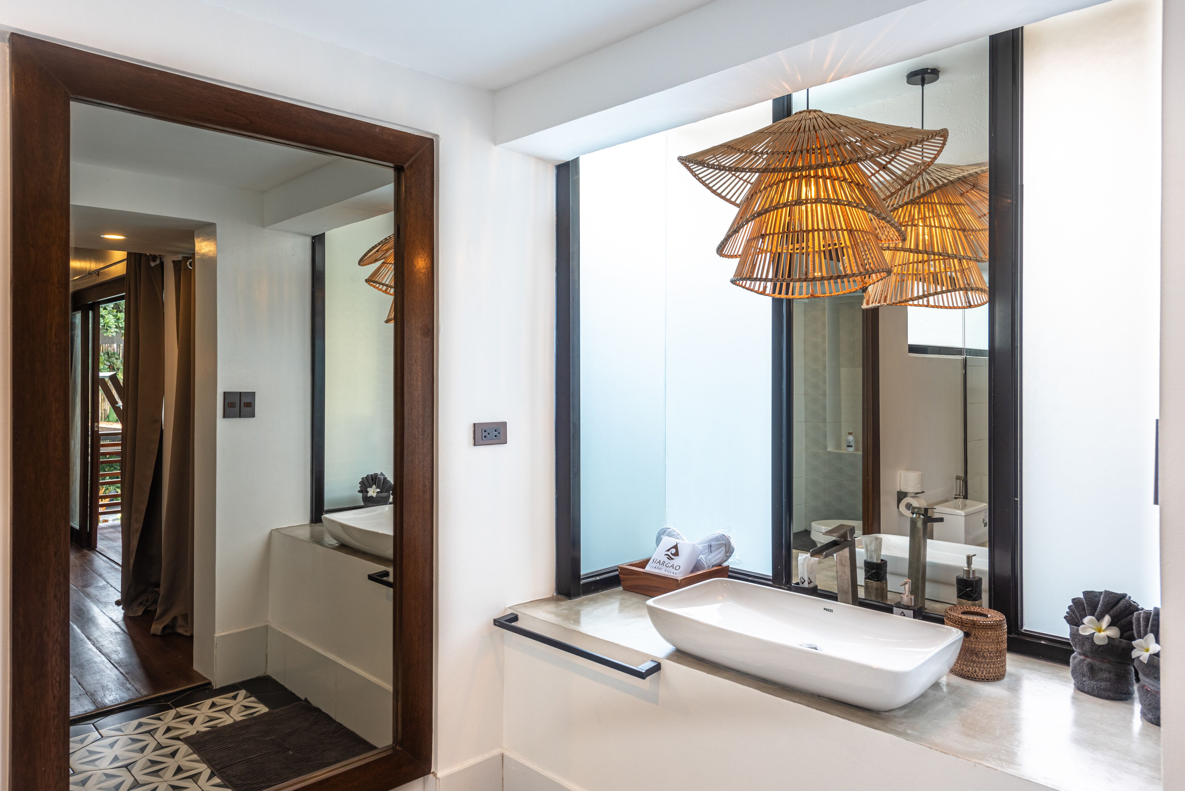 A modern bathroom with a large mirror, a white sink, and a unique woven light fixture.
