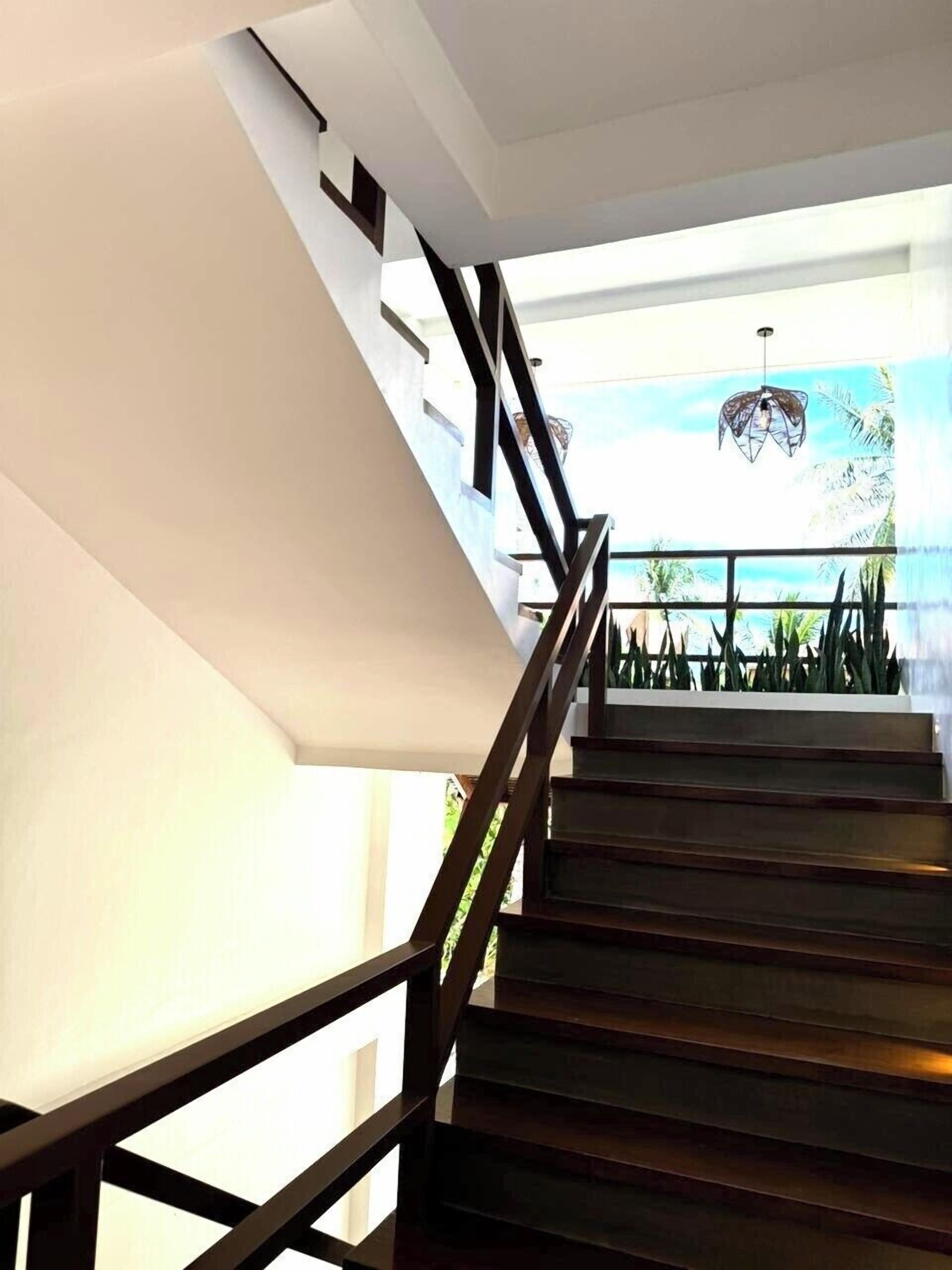 A staircase with wooden steps and black railings, leading to a room with a large window and a view of palm trees.