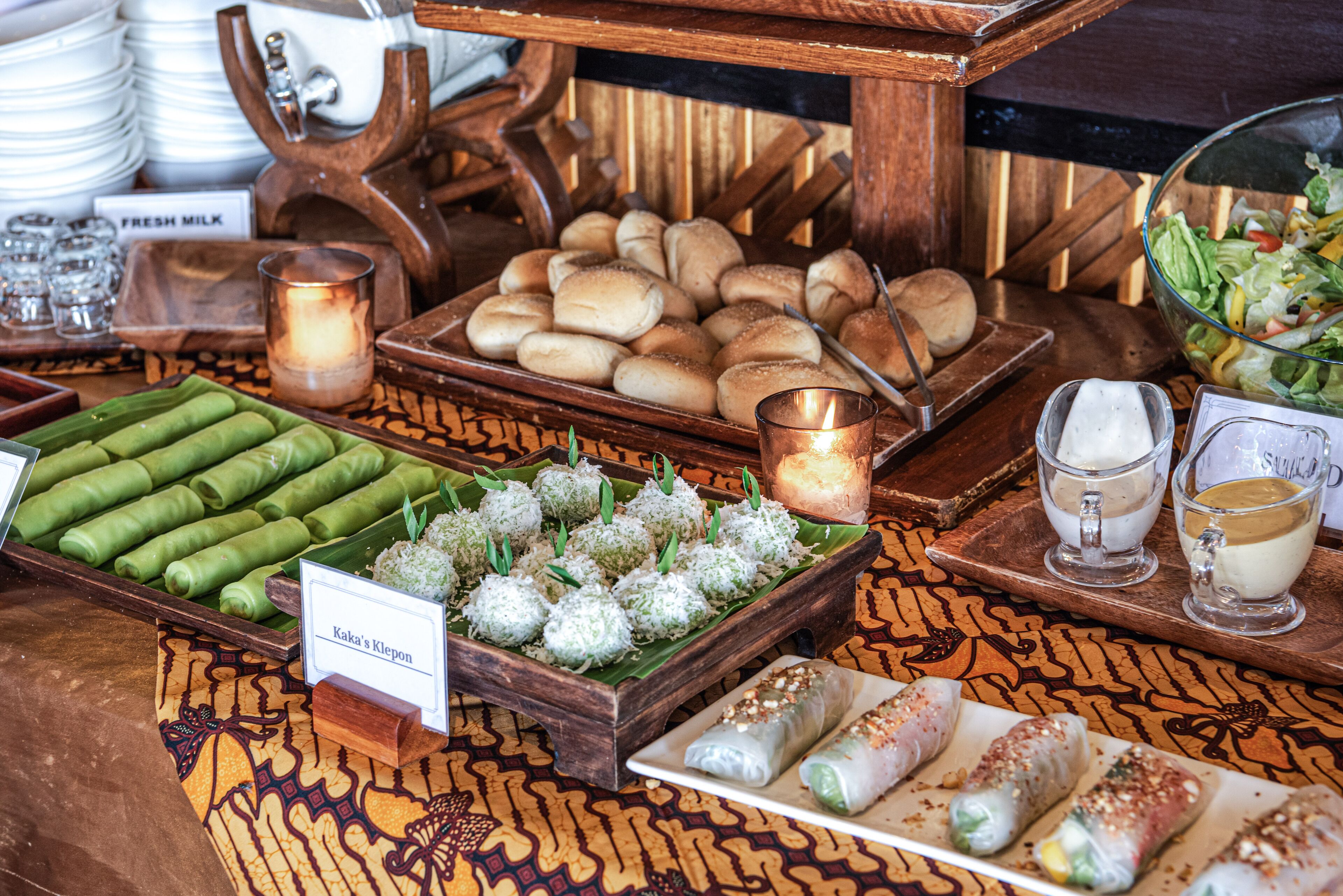 A buffet with various food items including rolls, spring rolls, and a salad.