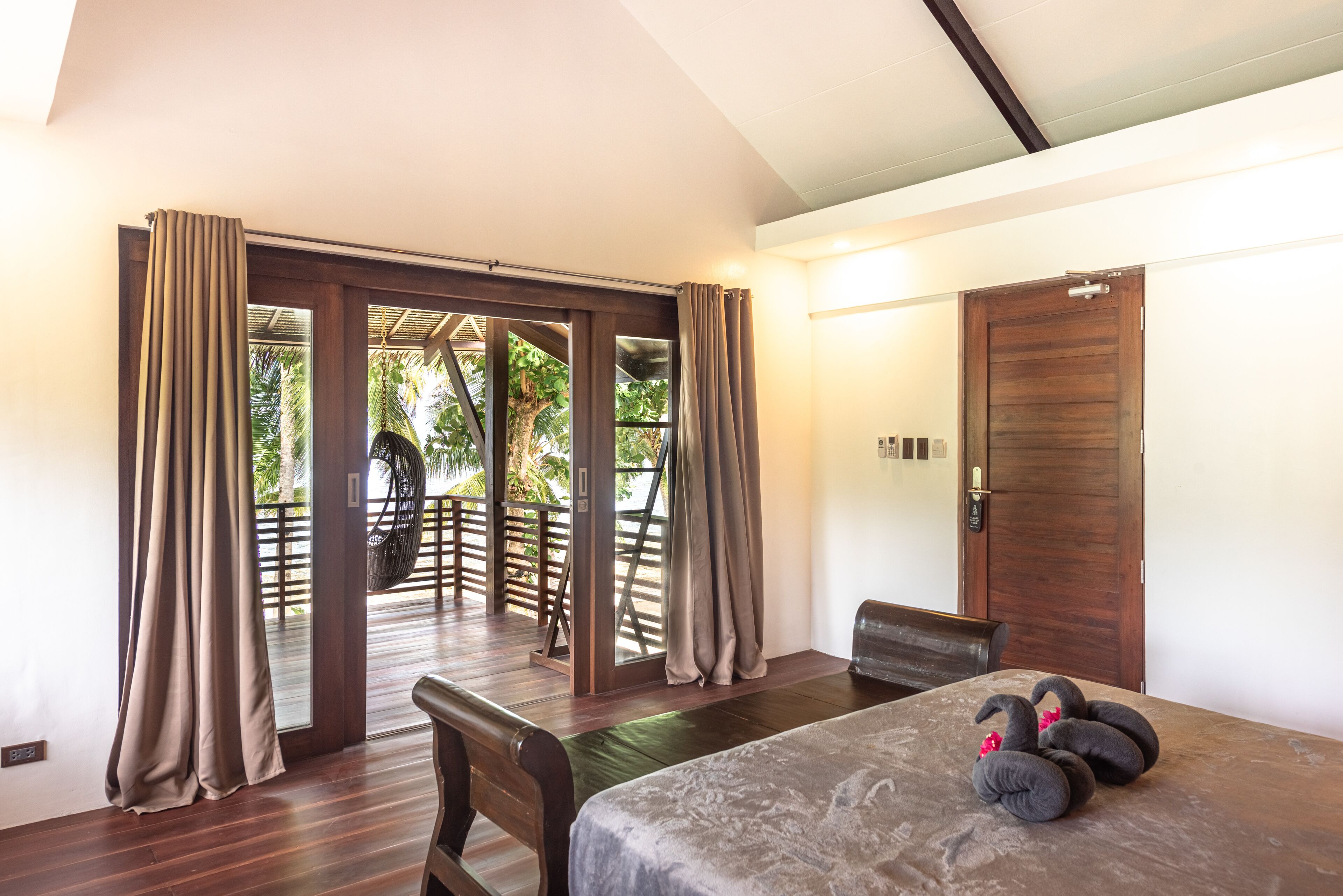 Une chambre avec un lit, des meubles en bois et une vue sur un jardin, visible à travers une porte vitrée.