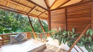 A wooden deck with a cushioned seating area, a slatted ceiling, and lush greenery in the background. - Siargao Island Villas (General Luna)
