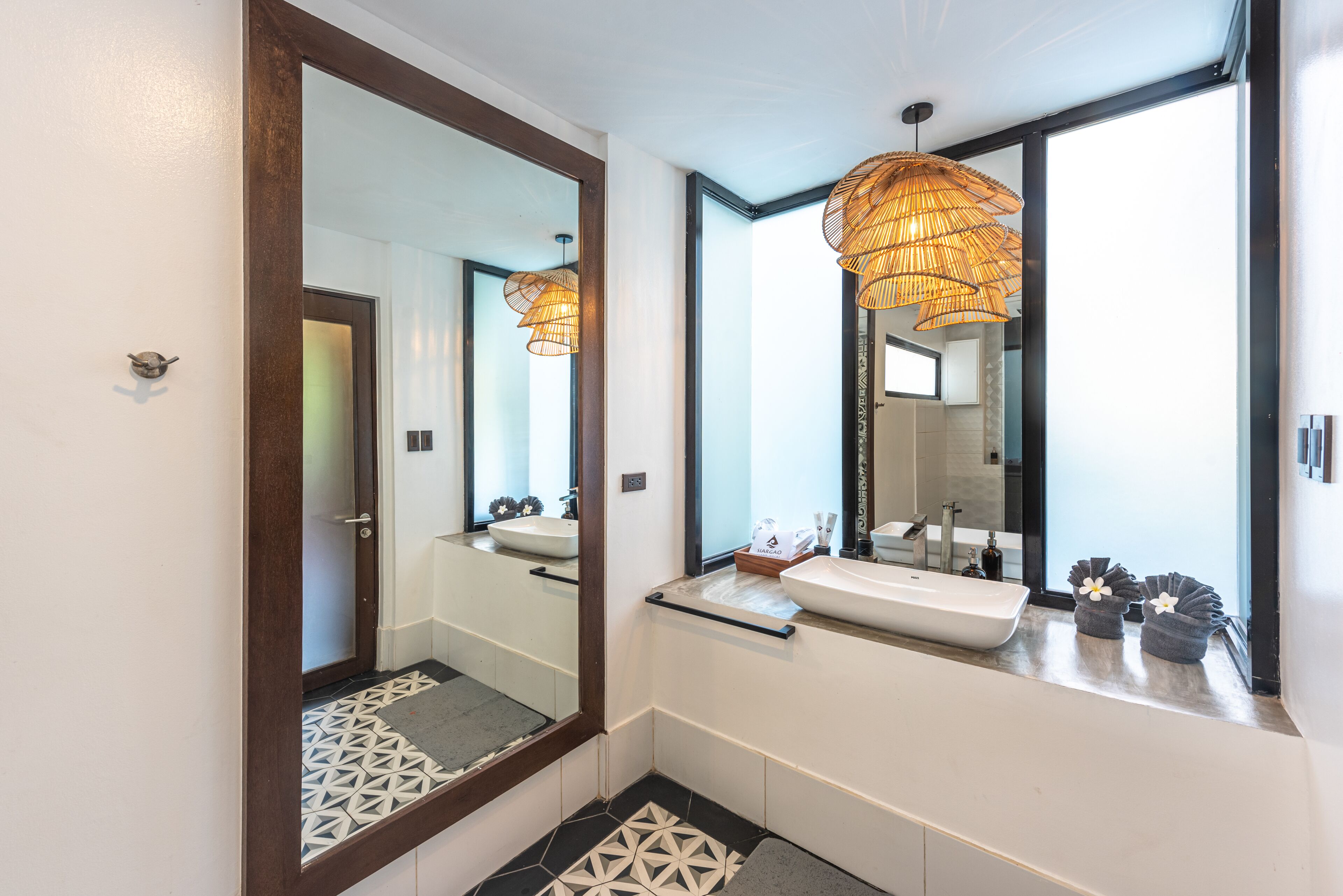 A modern bathroom with a large mirror, two sinks, and a geometric patterned floor.