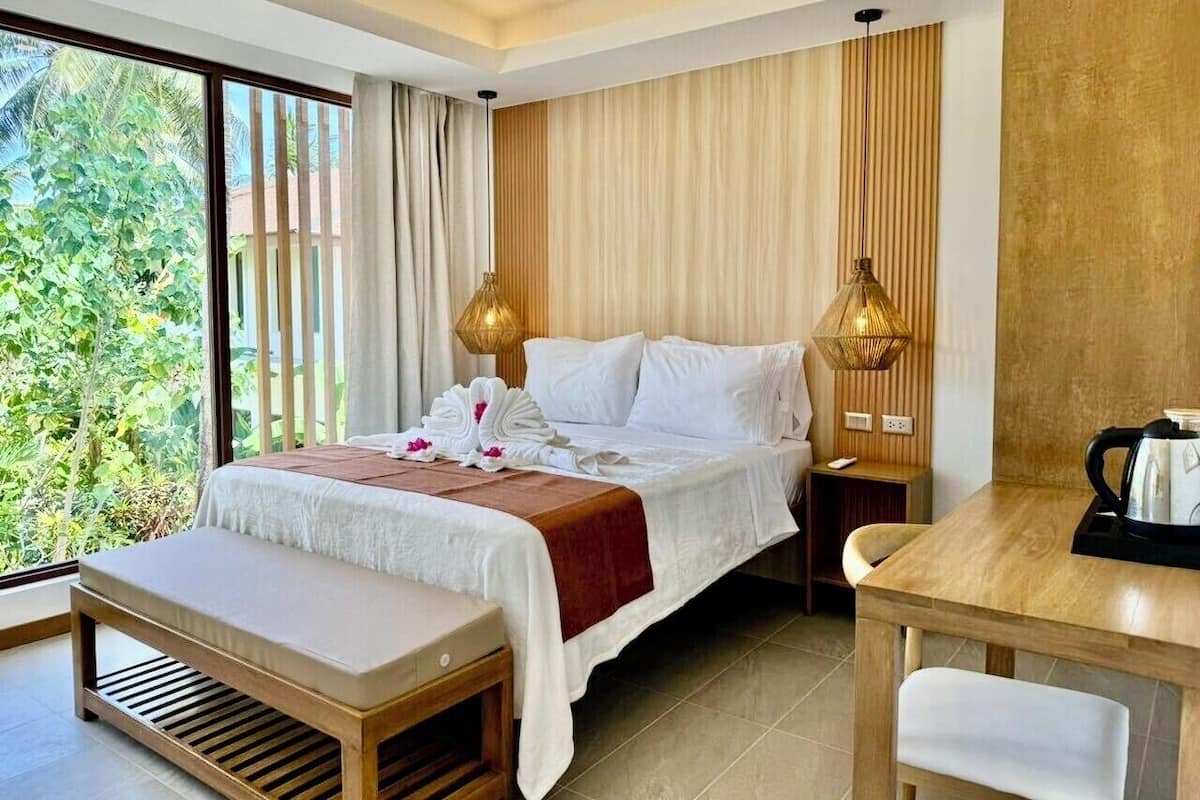 Ein Hotelzimmer mit einem Bett, Nachttischen, einem Schreibtisch und Blick auf Grünfläche.