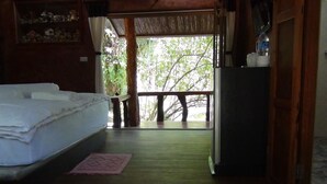 Una habitación con cama, una mesita, un refrigerador y vistas a árboles a través de una puerta de cristal.
